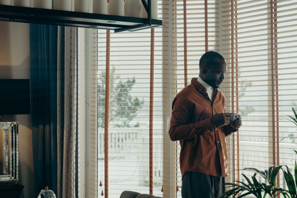 black man wearing brown jacket while looking through the window