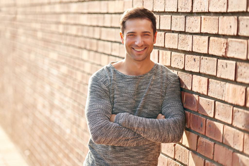 Single young man leaning against a wall with his arms crossed.