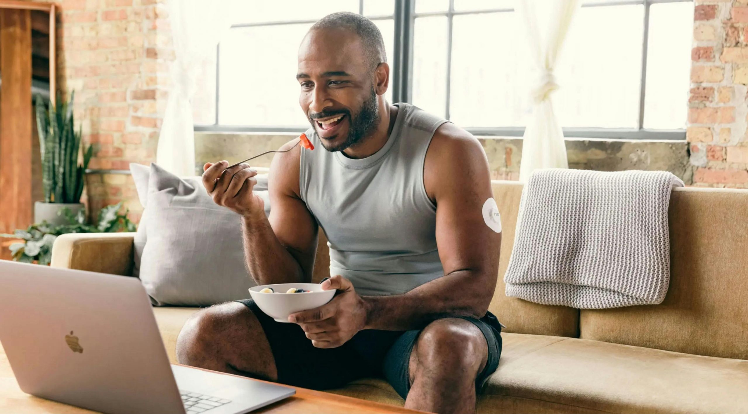 fit man eating a salad on a couch while watching something on his laptop